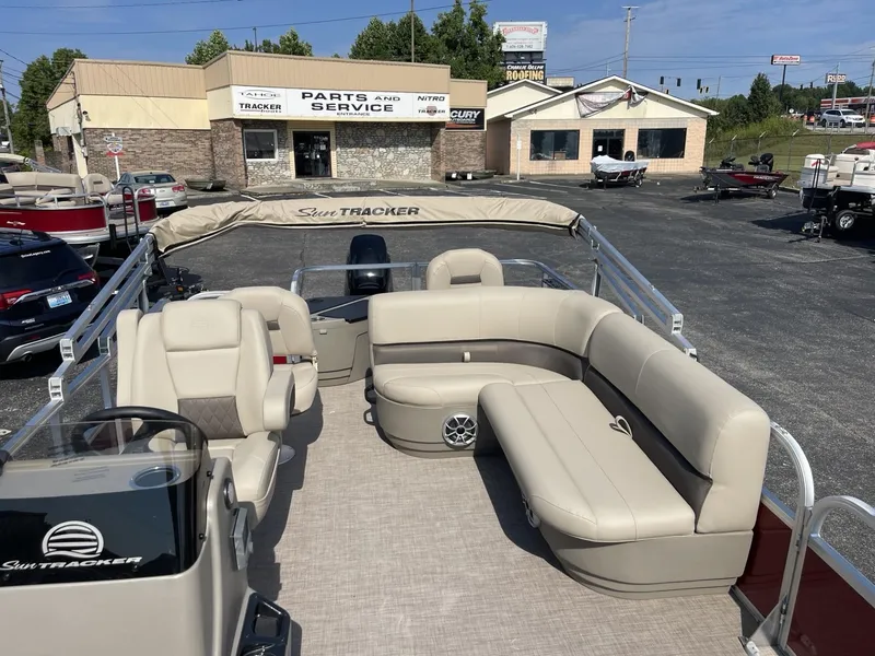 Slide: The Image of 2025 Sun Tracker Bass Buggy 18 DLX pontoon boat with beige seating, parked near service center. - 5