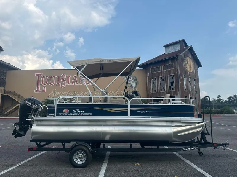 Slide: The Image of 2025 Sun Tracker Bass Buggy 18 DLX pontoon boat in parking lot. - 2