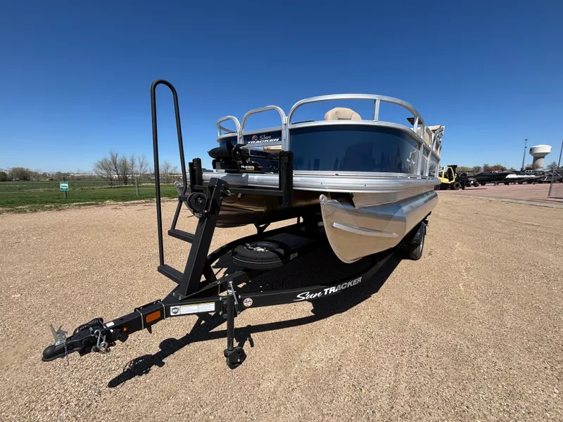 Slide: The Image of 2025 Sun Tracker Bass Buggy 16 XL Select pontoon boat on a trailer, parked outdoors. - 2