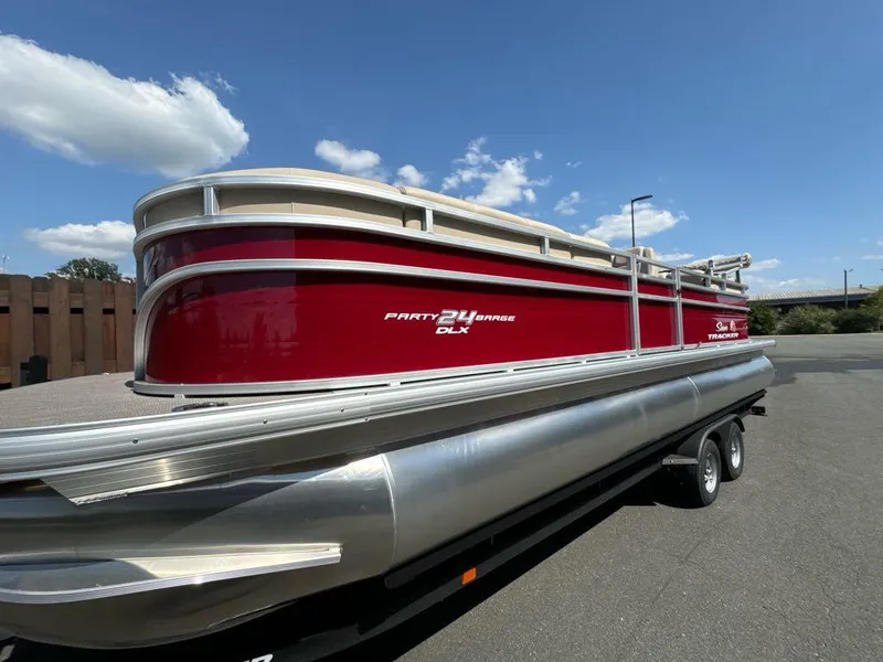 The Image of 2025 Sun Tracker Party Barge 24 DLX pontoon boat on trailer, red and silver design. - 0