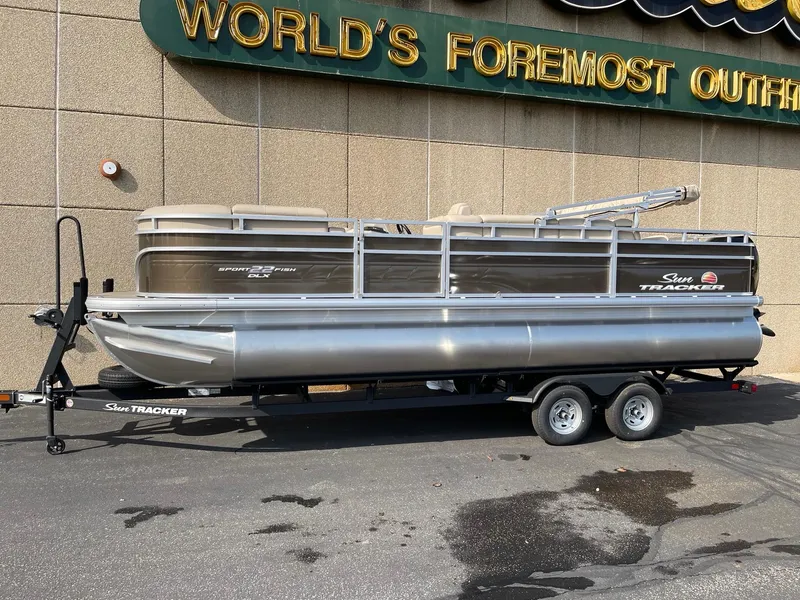 The Image of 2025 Sun Tracker SportFish 22 DLX pontoon boat on trailer, parked outdoors. - 0