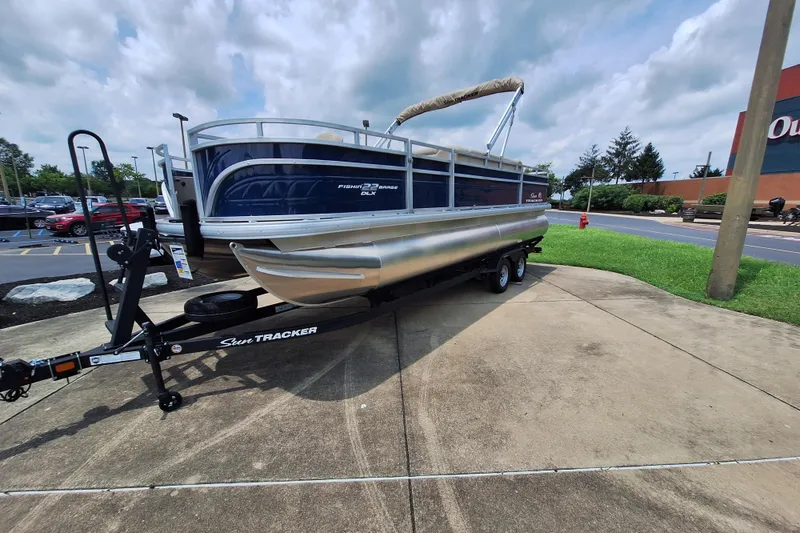 Slide: The Image of 2025 Sun Tracker Fishin' Barge 22 DLX pontoon boat on trailer, parked outdoors. - 3