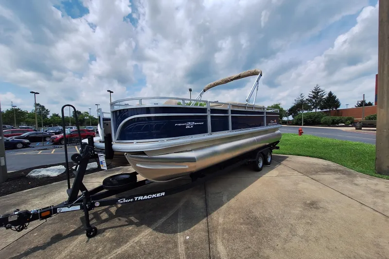 The Image of 2025 Sun Tracker Fishin' Barge 22 DLX pontoon boat on trailer, parked outdoors. - 0