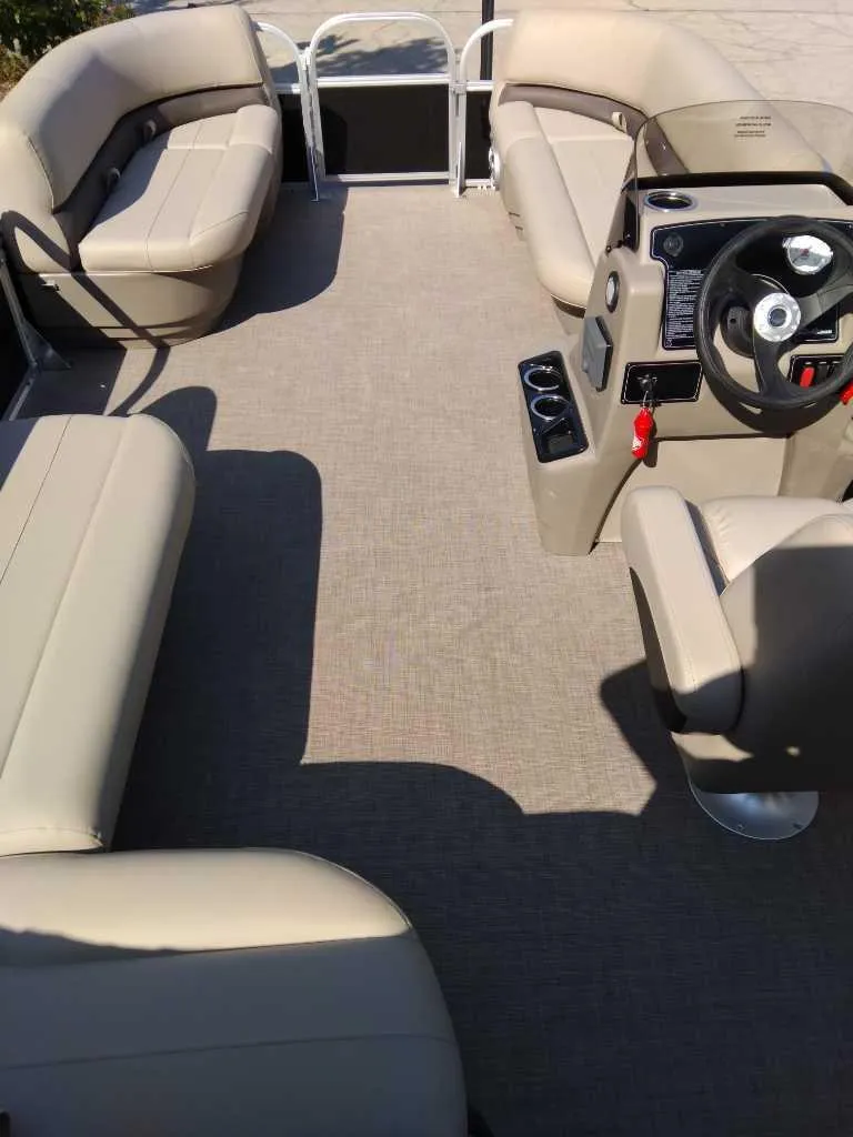 Slide: The Image of 2025 Sun Tracker Party Barge 16 DLX interior with beige seating and steering console. - 2