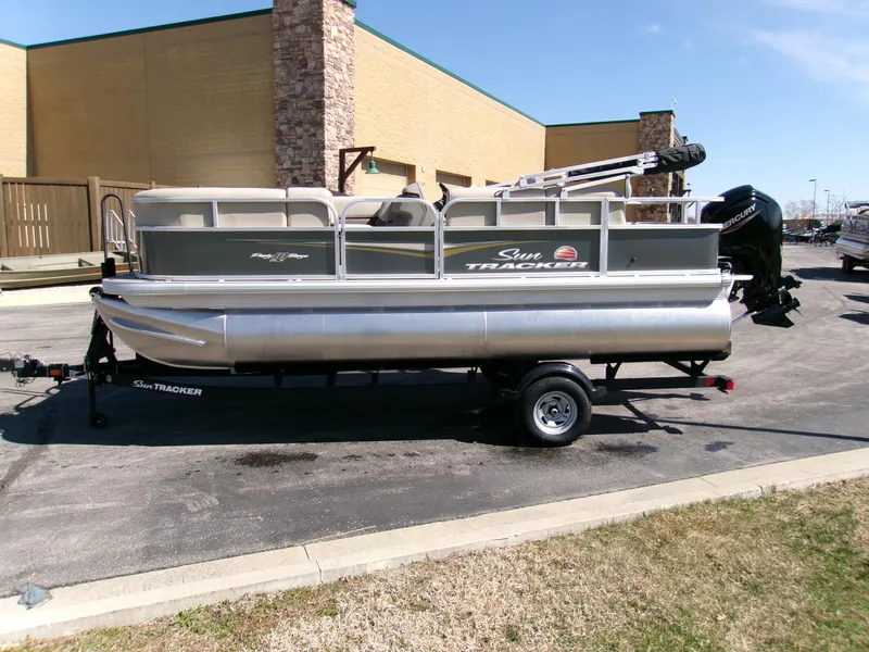Slide: The Image of 2025 Sun Tracker Party Barge 18 DLX pontoon boat on trailer, parked outdoors. - 2