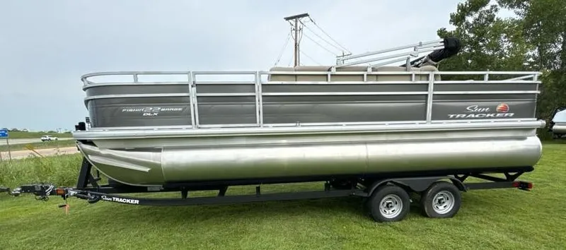 Slide: The Image of 2025 Sun Tracker Fishin' Barge 22 DLX pontoon boat on trailer, parked on grass. - 3