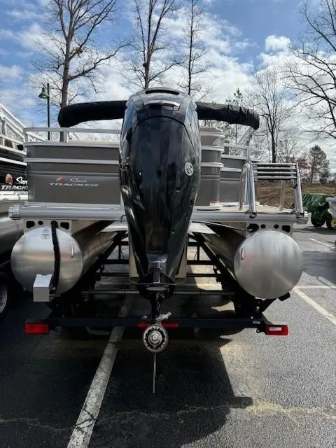 Slide: The Image of 2025 Sun Tracker Fishin' Barge 20 DLX pontoon boat, rear view with motor, parked outdoors. - 2