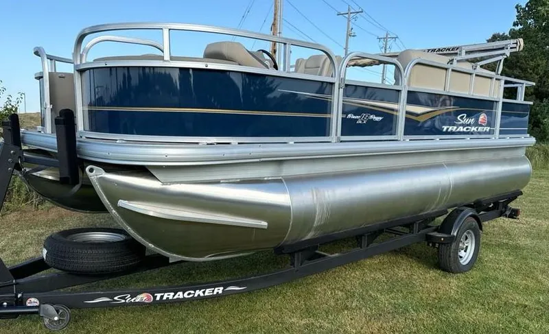 Slide: The Image of 2025 Sun Tracker Bass Buggy 18 DLX pontoon boat on trailer, parked on grass. - 2