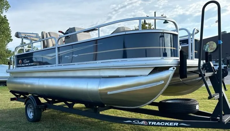 Slide: The Image of 2025 Sun Tracker Bass Buggy 18 DLX pontoon boat on trailer, parked on grass. - 5
