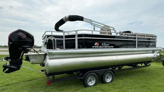 Slide: The Image of 2025 Sun Tracker SportFish 22 DLX pontoon boat on trailer, parked on grass. - 4