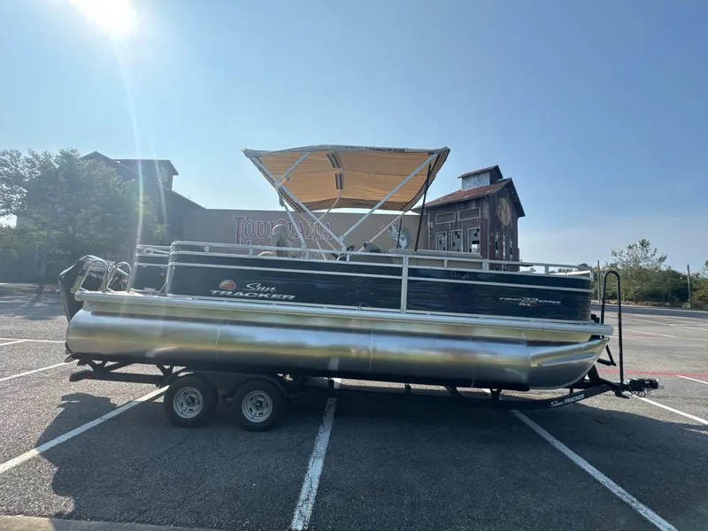 Slide: The Image of 2025 Sun Tracker Fishin' Barge 22 XP3 pontoon boat on trailer in parking lot. - 2