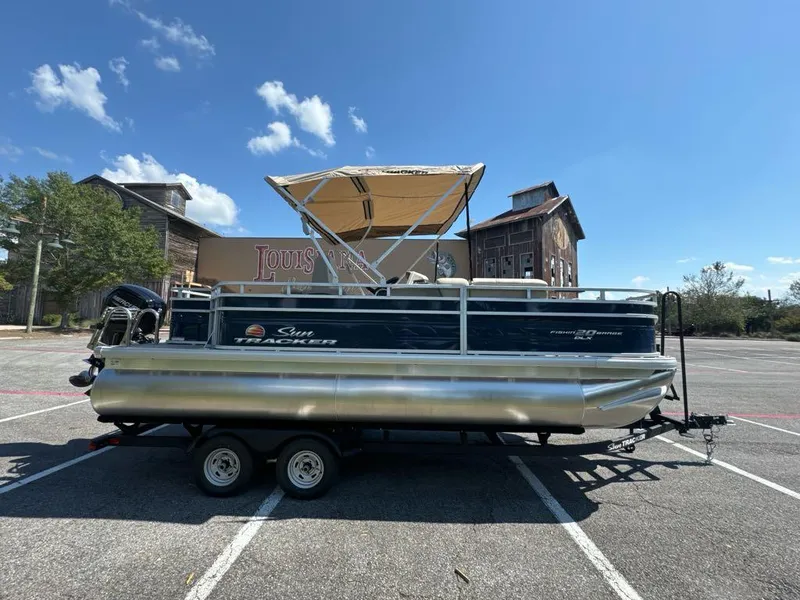 Slide: The Image of 2025 Sun Tracker Fishin' Barge 20 DLX pontoon boat parked in a lot under a clear blue sky. - 2