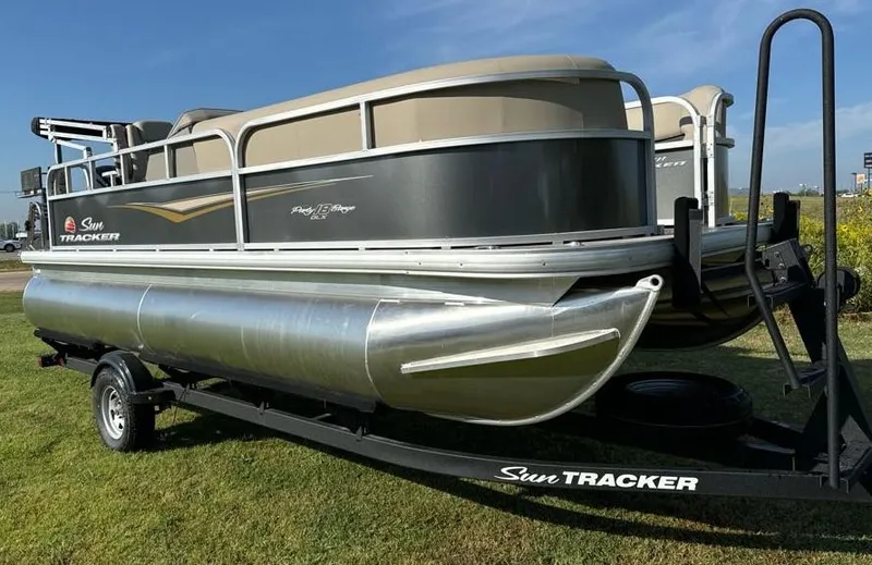 Slide: The Image of 2025 Sun Tracker Party Barge 18 DLX pontoon boat on trailer, parked on grass. - 4