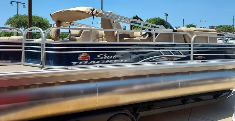 The Image of 2025 Sun Tracker Fishin' Barge 22 DLX pontoon boat, parked outdoors on a sunny day. - 0