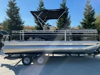 The Image of 2025 Sun Tracker SportFish 20 DLX pontoon boat on trailer, outdoors with trees in background. - 0