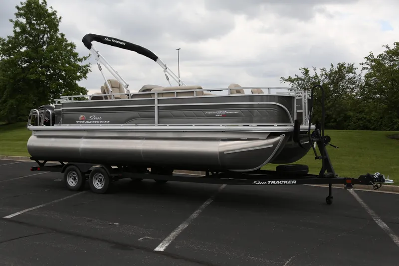The Image of 2025 Sun Tracker Fishin' Barge 22 XP3 pontoon boat on trailer in parking lot. - 0
