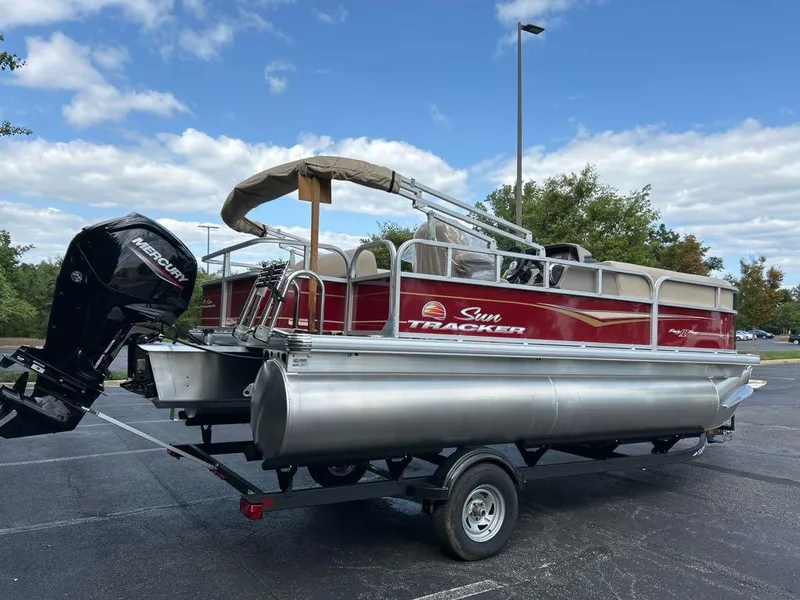 Slide: The Image of 2025 Sun Tracker Party Barge 18 DLX pontoon boat on trailer, parked outdoors. - 2