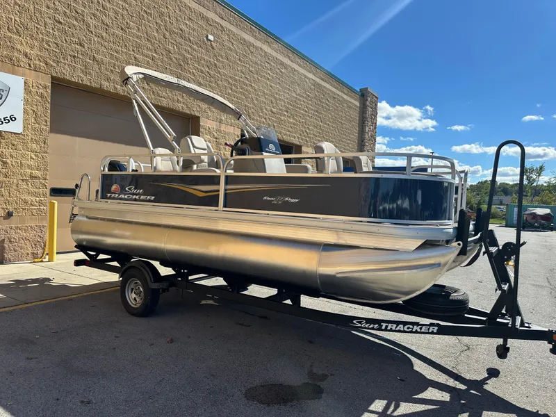 Slide: The Image of 2025 Sun Tracker Bass Buggy 18 DLX pontoon boat on trailer, parked outdoors. - 3