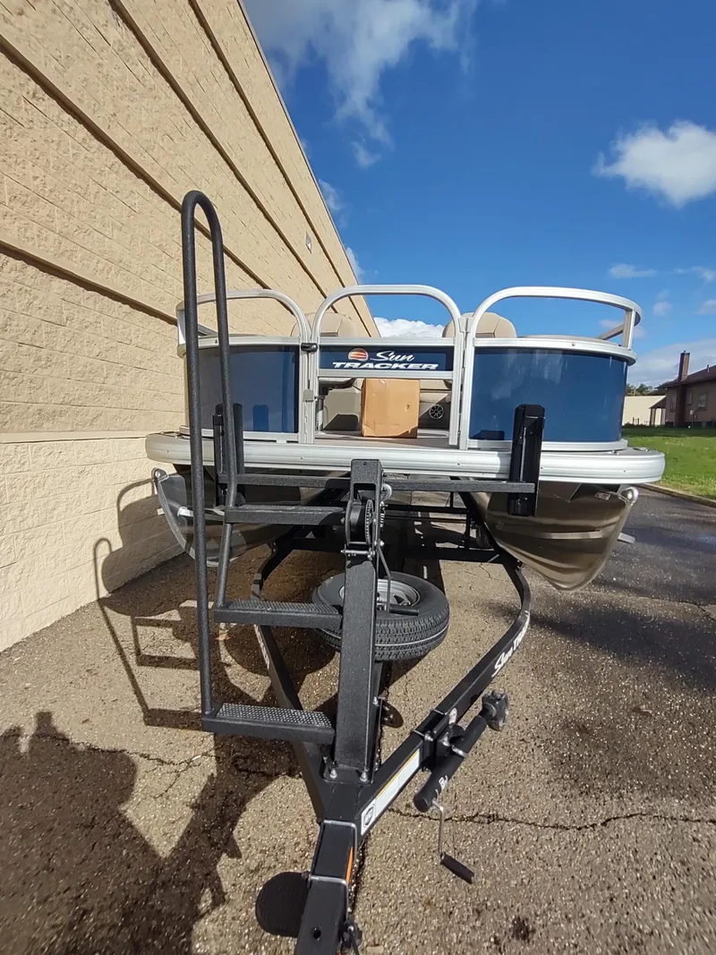 Slide: The Image of 2025 Sun Tracker Bass Buggy 18 DLX pontoon boat on trailer, parked outdoors. - 3