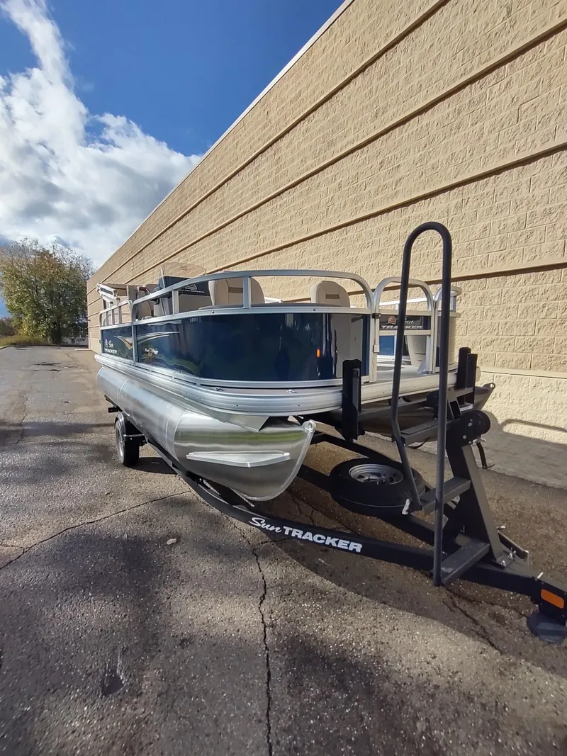 Slide: The Image of 2025 Sun Tracker Bass Buggy 18 DLX pontoon boat on trailer, parked outdoors. - 4
