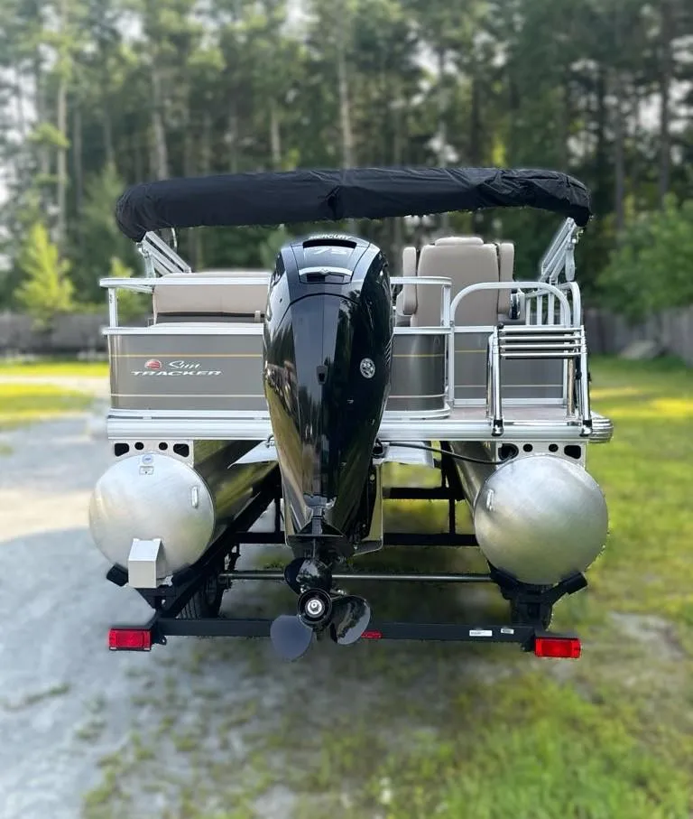 Slide: The Image of 2025 Sun Tracker Party Barge 18 DLX pontoon boat on trailer, parked outdoors. - 2