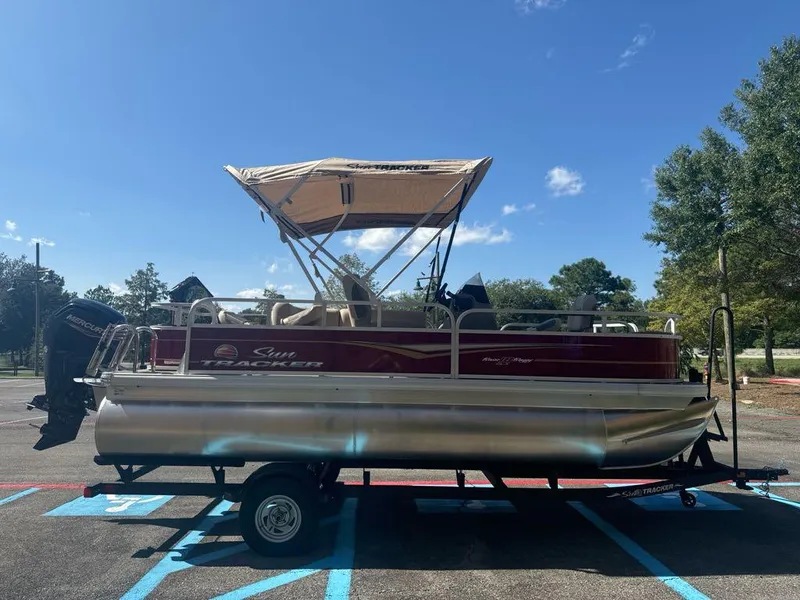 Slide: The Image of 2025 Sun Tracker Bass Buggy 18 DLX pontoon boat on trailer, parked outdoors. - 2