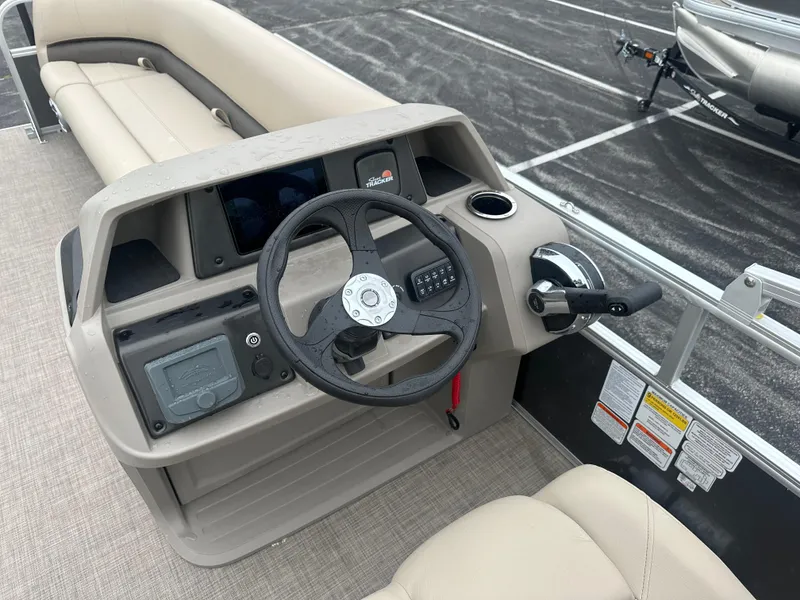 Slide: The Image of 2025 Sun Tracker Party Barge 18 DLX steering console with beige seating and controls. - 2