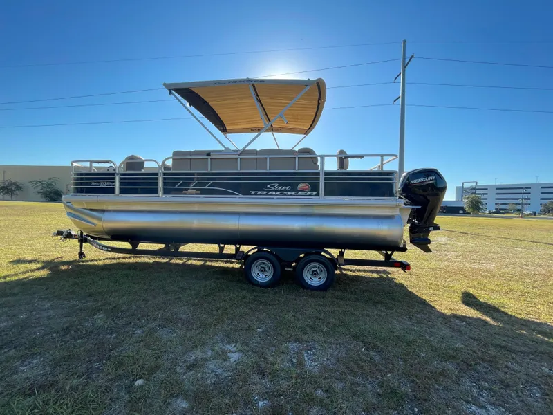 Slide: The Image of 2025 Sun Tracker Fishin' Barge 20 DLX pontoon boat on trailer, sunny day. - 2