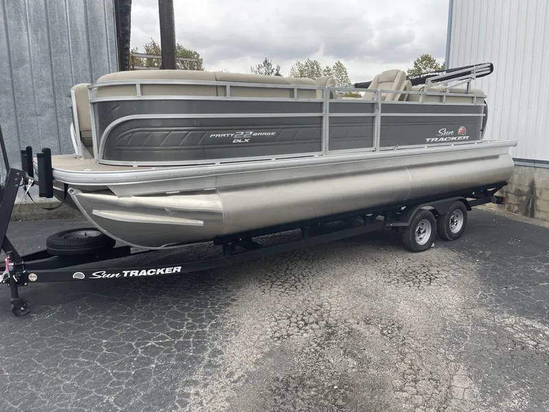 Slide: The Image of 2025 Sun Tracker Party Barge 22 DLX pontoon boat on trailer, parked outdoors. - 2