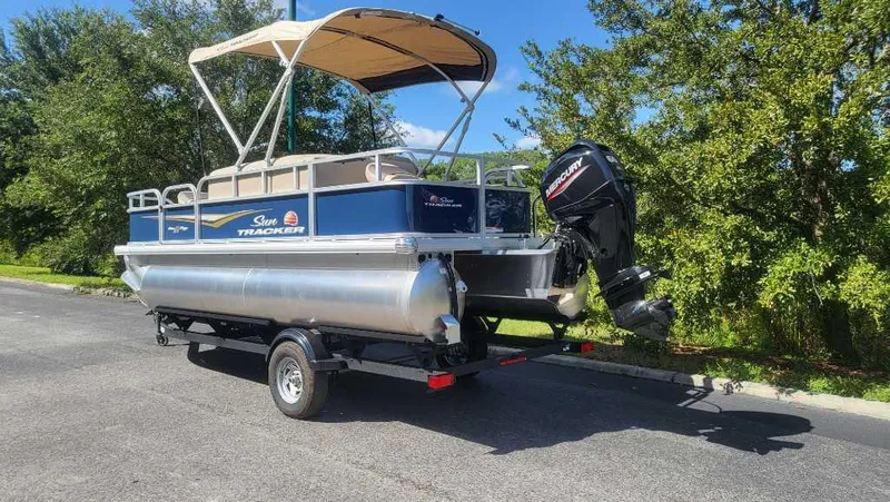 Slide: The Image of 2025 Sun Tracker Bass Buggy 18 DLX pontoon boat on trailer, parked outdoors. - 4