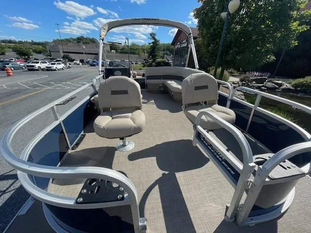 Slide: The Image of 2025 Sun Tracker Bass Buggy 16 XL Select pontoon boat with spacious seating in a parking lot. - 2