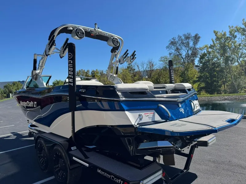 Slide: The Image of 2019 MasterCraft XT23 boat on trailer, parked outdoors under clear blue sky. - 5