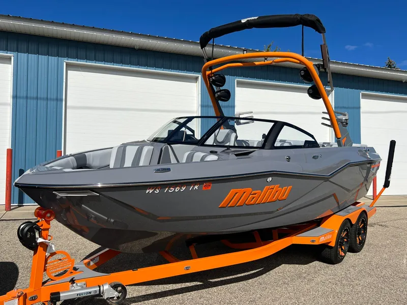 Slide: The Image of 2023 Malibu Wake Setter LSV 22 boat on orange trailer, parked near blue building. - 32