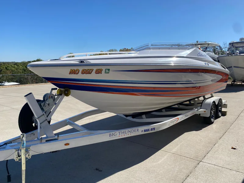 Slide: The Image of 2019 Baja 24 Outlaw speedboat on trailer, vibrant stripes, sunny day. - 2