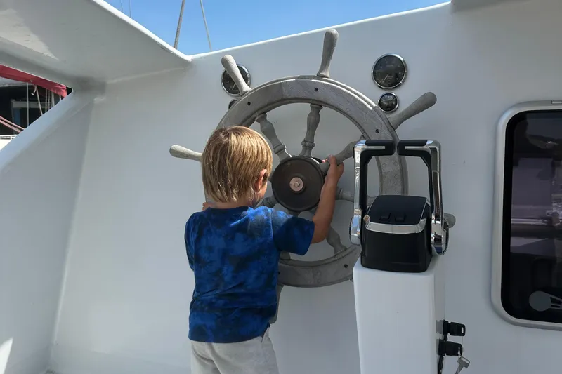 Slide: The Image of Child steering a 2019 Kelsall 38ma boat, holding the wheel on a sunny day. - 32