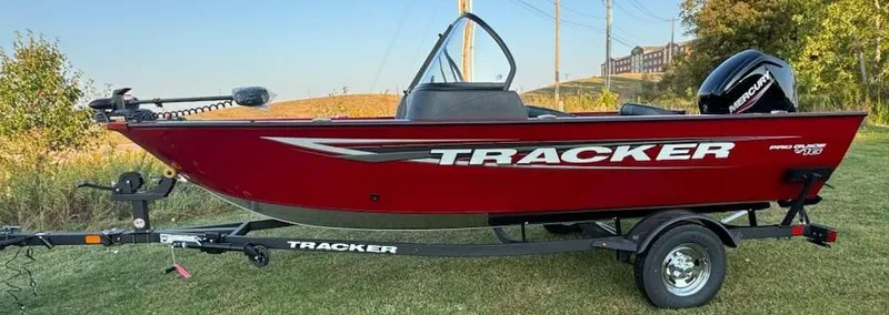Slide: The Image of 2025 Tracker Pro Guide V-16 WT boat on trailer, red exterior, parked on grass. - 2