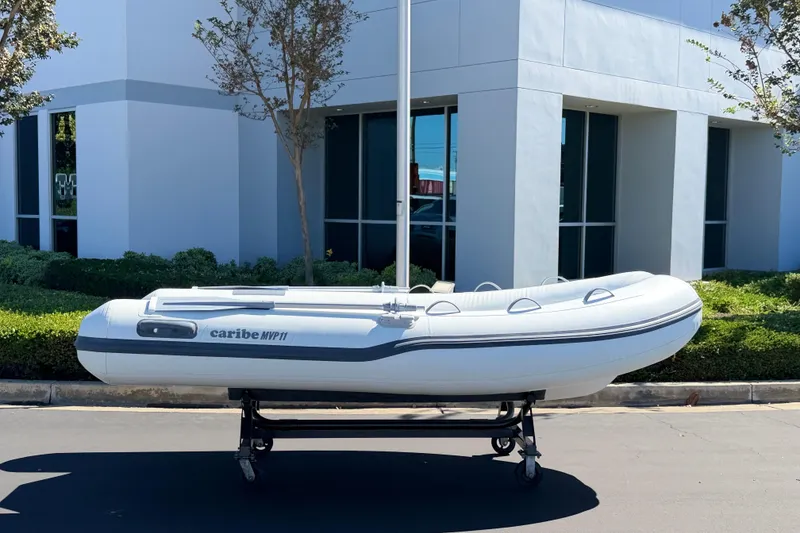 Slide: The Image of Inflatable Caribe MVP11 boat on a wheeled stand, 2025 model, outside modern building. - 18