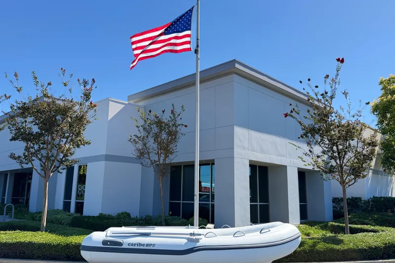 Slide: The Image of Inflatable Caribe MVP11 boat, 2025 model, displayed outside modern building with American flag. - 3