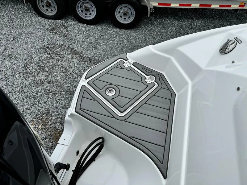 Slide: The Image of 2025 NauticStar 243 DC Deck boat, white hull with gray deck, parked on gravel. - 11