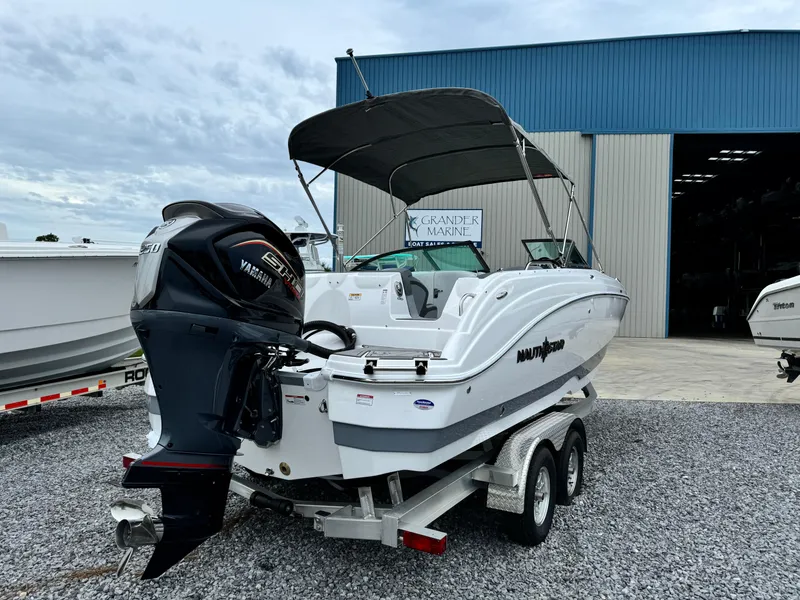Slide: The Image of 2025 NauticStar 243 DC Deck boat on trailer, parked outside a marine warehouse. - 5