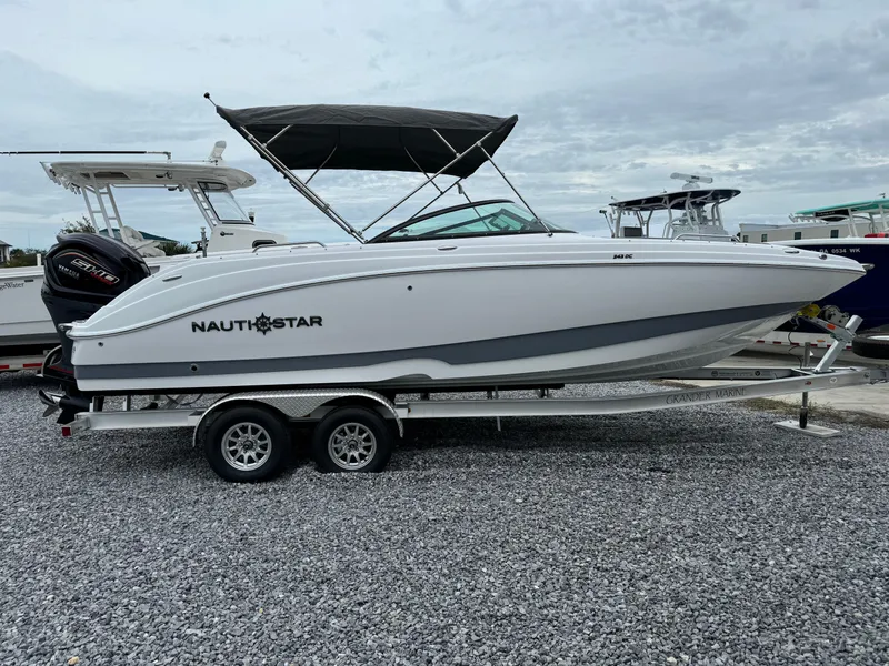 Slide: The Image of 2025 NauticStar 243 DC Deck boat on trailer, parked on gravel lot. - 7