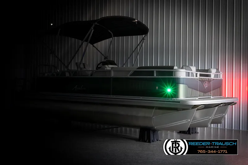 Slide: The Image of 2025 Avalon VENT CRB pontoon boat in dimly lit showroom with green navigation light. - 4