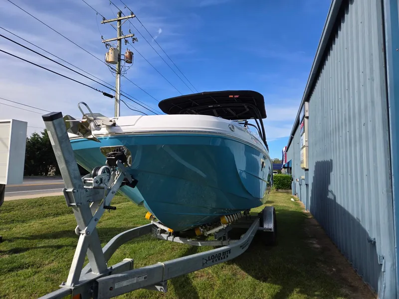 Slide: The Image of 2025 Hurricane SunDeck 2600 OB boat on trailer, parked beside a blue building. - 9