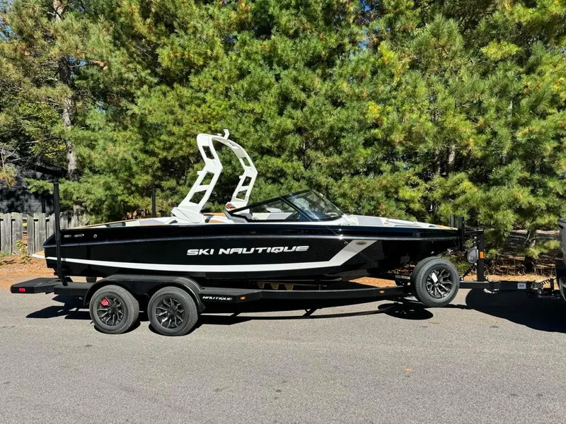 The Image of 2025 Nautique Ski 200 Open Bow boat on trailer, parked near trees. - 0