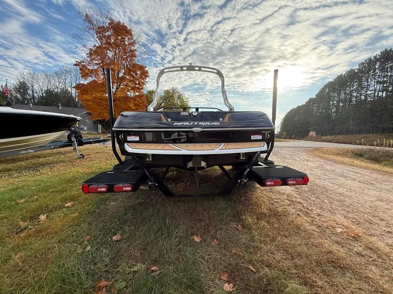 Slide: The Image of 2025 Nautique Ski 200 Open Bow boat on grassy area, autumn trees in background. - 45