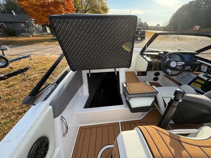 Slide: The Image of 2025 Nautique Ski 200 Open Bow interior with open storage compartment, modern dashboard, and wood accents. - 49
