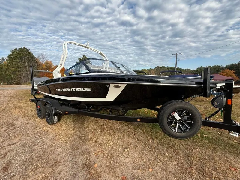 Slide: The Image of 2025 Nautique Ski 200 Open Bow boat on trailer, parked outdoors under cloudy sky. - 5
