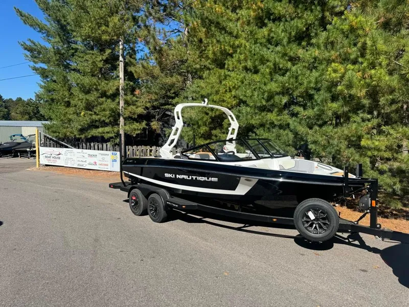 Slide: The Image of 2025 Nautique Ski 200 Open Bow boat on trailer, parked near trees. - 6