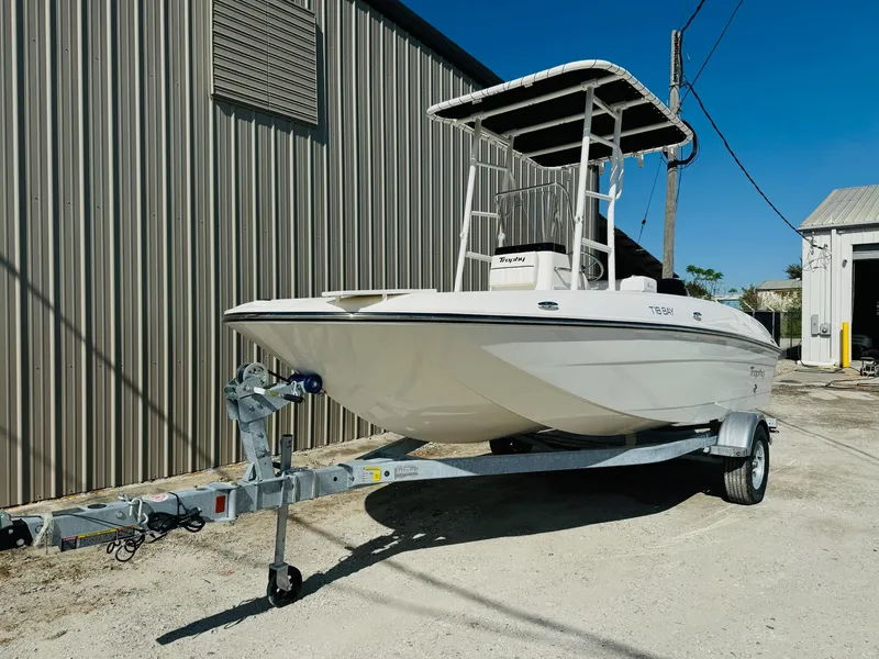 Slide: The Image of 2025 Bayliner Trophy T18 boat on trailer, parked outdoors near a metal building. - 1
