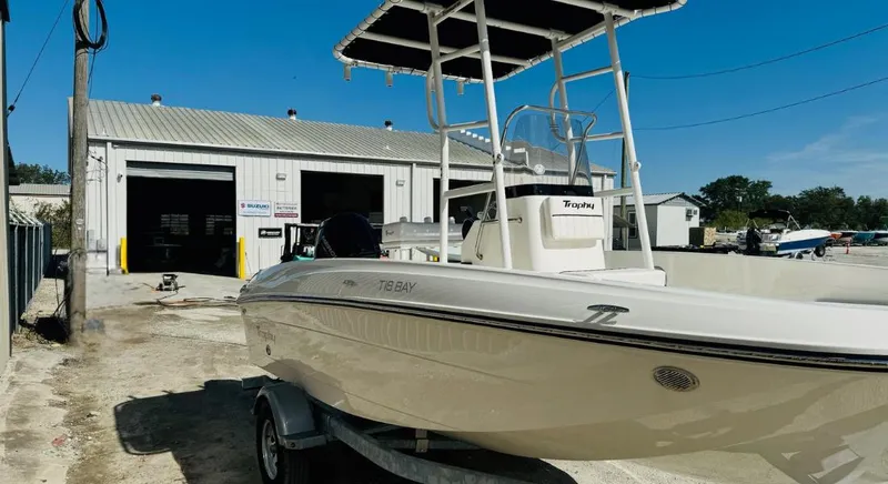 Slide: The Image of 2025 Bayliner Trophy T18 boat on trailer outside a workshop under clear blue sky. - 4